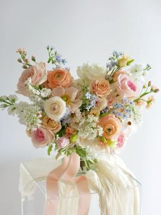 a vase filled with lots of flowers on top of a white table next to a pink ribbon