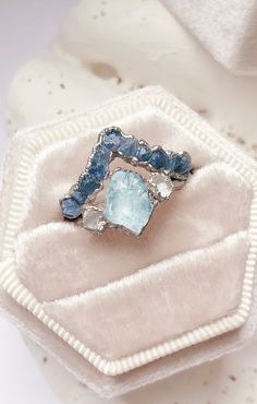 a ring with blue and white stones on it sitting on a cloth bag next to a pair of scissors