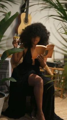 a woman sitting on a chair reading a book and holding a guitar in her hand