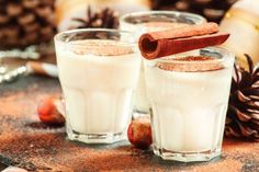 two glasses filled with white liquid and cinnamon on top of a table next to pine cones