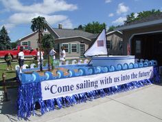 some people are standing in front of a sailboat on the street with blue streamers