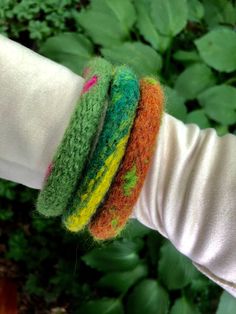 a woman's arm with three colorful bracelets on top of each other in front of green plants