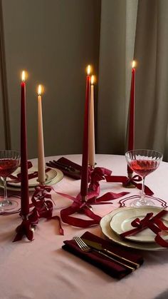 a table topped with candles and plates covered in red ribbon next to two wine glasses