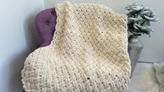 a white knitted blanket sitting on top of a purple chair