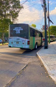 a green and white bus on street next to lamp post with no parking sign in front