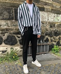 a man standing in front of a stone wall wearing a striped shirt and black pants