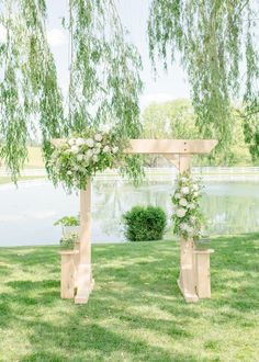 an outdoor ceremony setup with white flowers and greenery on the grass near a lake