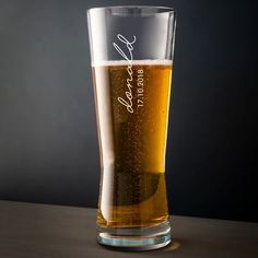 a tall glass filled with beer sitting on top of a wooden table next to a black wall