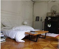 a bed sitting on top of a hard wood floor next to a table with books