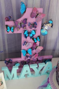 a purple and blue number one with butterflies on it sitting next to a cupcake