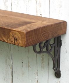 a wooden shelf with metal brackets and a clock on the top, against a white painted wall