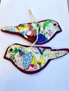 two birds made out of fabric sitting on top of a piece of white paper next to each other