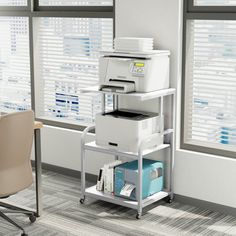 a desk with a printer and other office supplies on it in front of large windows