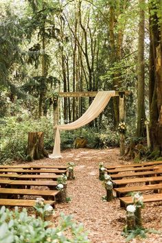 an outdoor ceremony set up in the woods with wooden benches and white draping