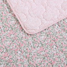 a pink and green flowered blanket laying on top of a bed