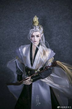 a doll dressed in white and black holding a stick with gold accents on it's head