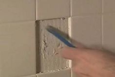 a person is using a blue pen to paint a tile wall with white grout