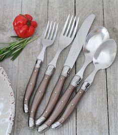 four forks, two spoons and one knife on a wooden table next to a red flower