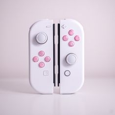 two nintendo wii game controllers sitting side by side on a white surface with pink buttons