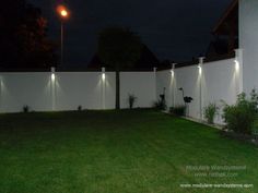 a fenced in yard with lights on the top of it and grass around it