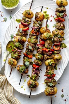 a white plate topped with meat and veggies on skewers next to a bowl of pesto sauce