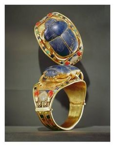 two gold rings with blue and red stones on them, one in the shape of an egg