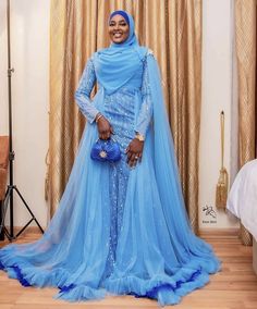 a woman in a blue dress and head scarf posing for the camera with her purse