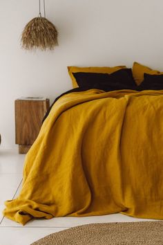 a bed with yellow sheets and pillows in a white room next to a wooden table