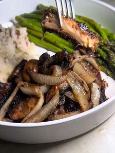 a white plate topped with meat and veggies next to mashed potatoes, asparagus