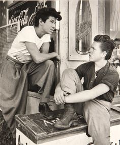 two young men sitting on the back of a train car talking to each other in front of a coca cola machine