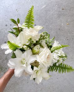 a bouquet of white flowers and greenery in someone's hand on the ground