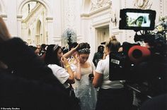 a woman in a white dress is surrounded by people and cameras as she walks down the aisle