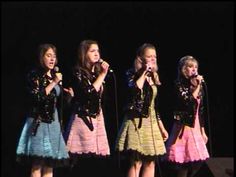 four girls singing into microphones on stage