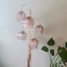 a lamp with five pink glass flowers on it next to a potted plant in the corner