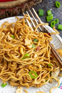 a plate full of noodles with chopsticks on the side and chopped green onions