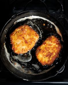 two pieces of fried fish cooking in a skillet on the stove top with oil