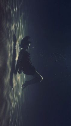 a woman standing in the water with her legs spread out and head down, looking up