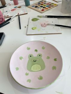 a bowl with an animal painted on it sitting on a table next to paintbrushes and watercolors