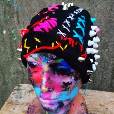 a person with colorful paint on their face and head wearing a black knitted hat