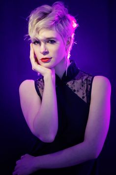 a woman posing with her hand on her chin and looking at the camera while wearing a black dress