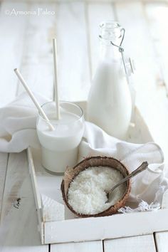 coconuts and milk are sitting on a white wooden tray with two spoons next to them