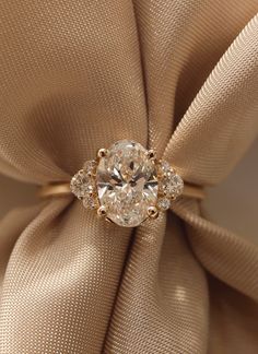 a diamond ring sitting on top of a beige cloth with a satin bow around it