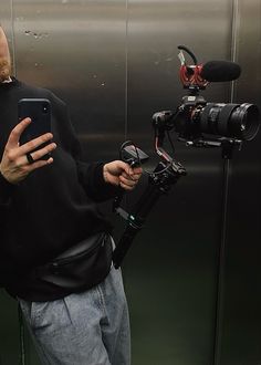 a man standing in front of a camera holding a cell phone and recording something on a tripod