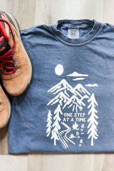 One Step At A Time T-Shirt | Still Wild Free Co. - Life is a whole lot easier when you take one step at a time... and add some hiking in the mixture! Give yourself this reminder and inspire others to do the same with this one-of-a-kind design printed on cozy Comfort Color t-shirts, garment-dyed to create a long lasting soft and comfortable t-shirt. #mountaintshirt #outdoorgraphictee #adventuretshirt #motivationaltee #foresttshirt #hikingtshirt #hikers #outdoortshirt #natureinspiredtshirt Tshirt Style Outfit, Creative T Shirt Design, Wardrobe Makeover, Tshirt Printing Design, Hiking Tshirt, One Step At A Time, Wild Free, Outdoor Shirt, Graphic Tee Design