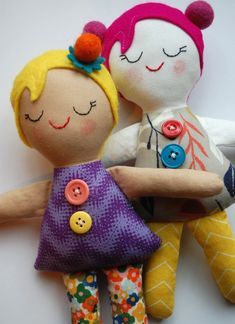 two stuffed dolls sitting next to each other on a white surface with one holding the other's hand