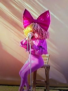 a woman sitting on top of a chair wearing a pink outfit and holding a microphone