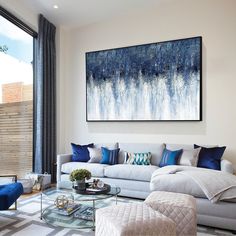 a living room filled with furniture and a large painting on the wall above it's glass coffee table