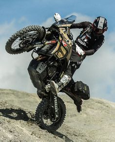 a man riding on the back of a dirt bike down a rocky hill with clouds in the background