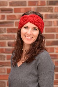 a woman wearing a red headband standing in front of a brick wall smiling at the camera