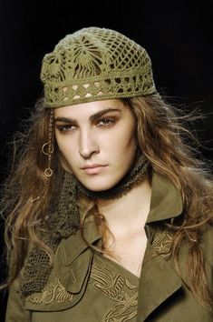 a woman with long hair wearing a green hat and scarf on the catwalk at london fashion week